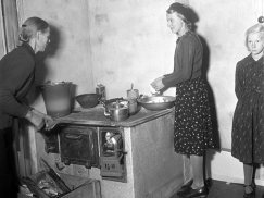 Kuva: Honkasen perheen naiset ovat keittiössä uuden lieden ääressä. Vasemmalla emäntä, Hedvig Honkanen, keskellä Aino-tytär ja oikealla yksi lapsista.(1940) Yle kuvapalvelu.
