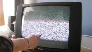 Kuvassa vanhan mallinen televisio, josta näkyy "lumisadetta". Kuvassa vasemmalla ihmisen kädessä oleva kaukosäädin.