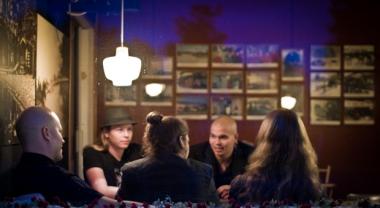 ?Verify-yhtyeen jäsenet kuvattuna ravintolassa. Viisi miestä istuu pöydän ääressä ja keskustelee. Juomia ei ole kuvattu.