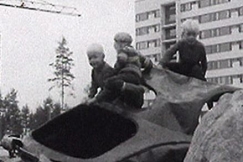 Kuva: Kolme pient poikaa leikkii auton romulla kerrostalotymaalla. YLE kuvanauha.