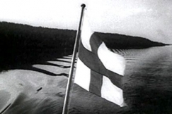 Kuva: Suomen lippu liehuu jrvimaisemassa (1930-luku). Aho & Soldan /YLE.